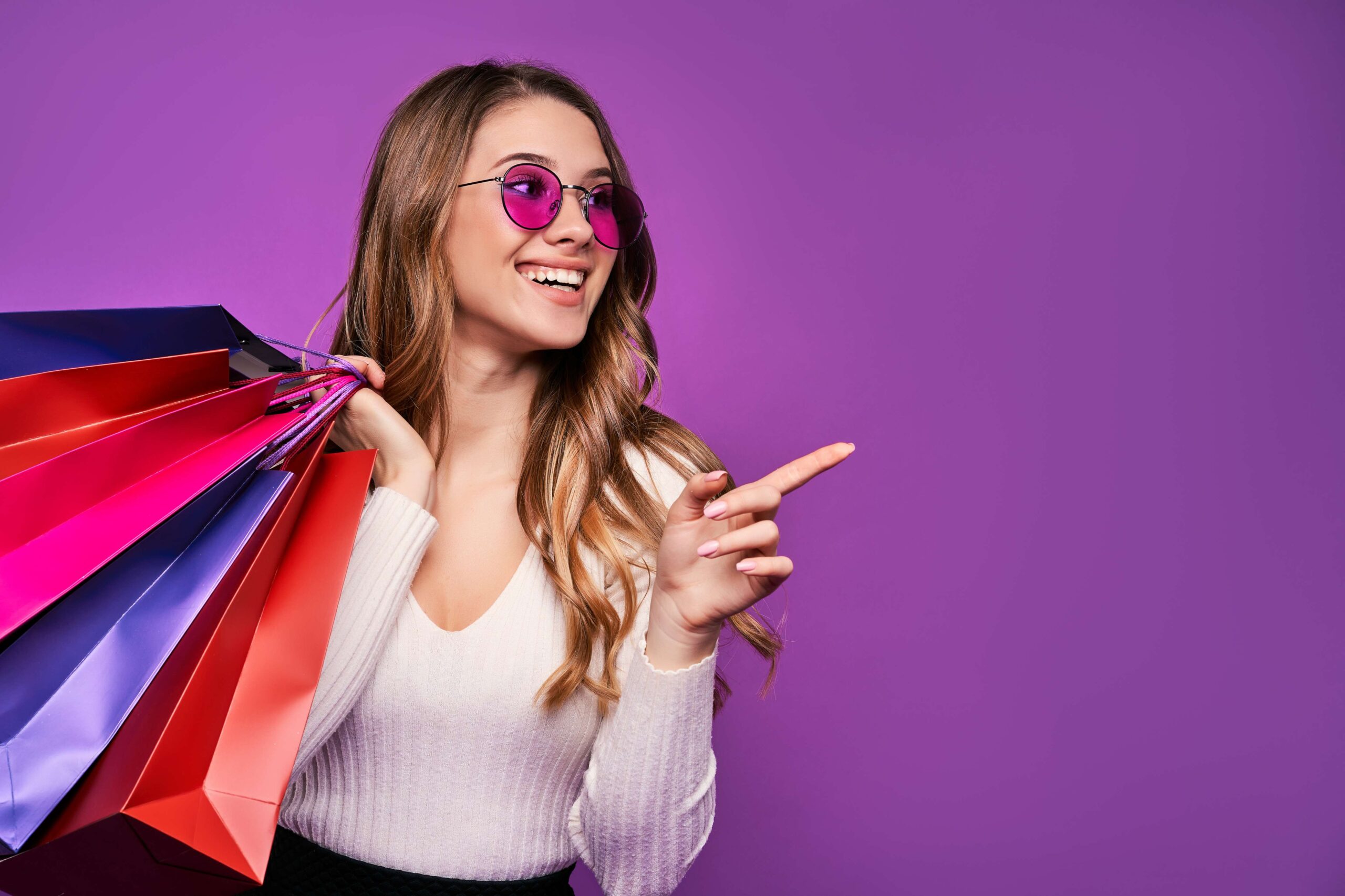 beautiful-smiling-young-blonde-woman-pointing-sunglasses-holding-shopping-bags-credit-card-pink-wall-compressed (1)